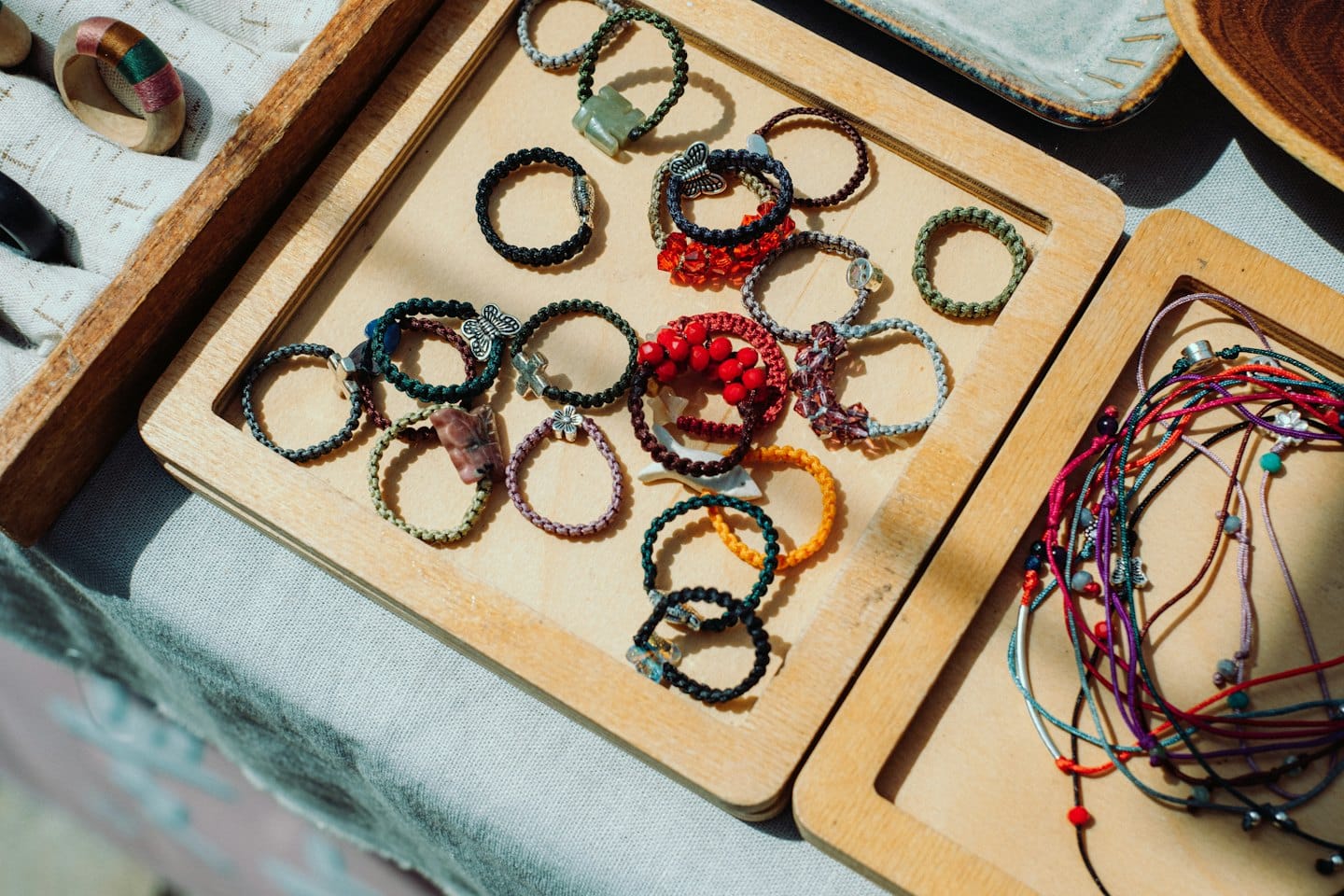 Handmade braided bracelets and beaded necklaces displayed in wooden trays.